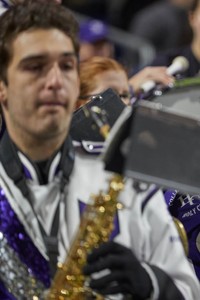 A Holy Cross trombone player performing while wearing a purple and white marching band uniform.