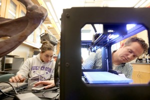 A student watches as a professor concentrates on using a scanning device in a laboratory setting.