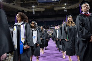 Smiling students in cap and gown as they walk down the aisle during commencement.