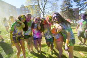 Six female students smile for the camera while outside covered head to toe in colorful paint.