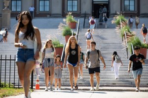 Students smiling as they walk on campus with the steps to Dinand library in the background.