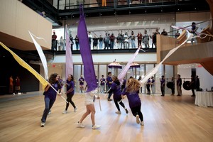 Six students holding colorful flags run in a circular pattern during a performance at the Prior Performing Arts Center