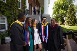 Five students laugh while being photographed wearing graduation gowns and regalia.