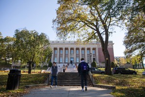 Two male students pictured strolling in opposite directions down a path with Dinand Library in the background.