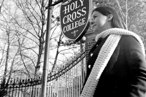 A black and white historical image showing a young woman looking away from the camera while  standing in front of a Holy Cross sign.