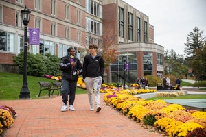 Two male students walk down a path on campus with the Hogan Campus Center visible in the background.