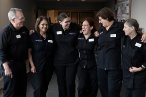Six dining services staff members in black uniforms standing side by side while smiling and laughing.
