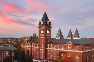 The clock tower of O’Kane Hall pictured during sunset with pink and purple clouds in the background.